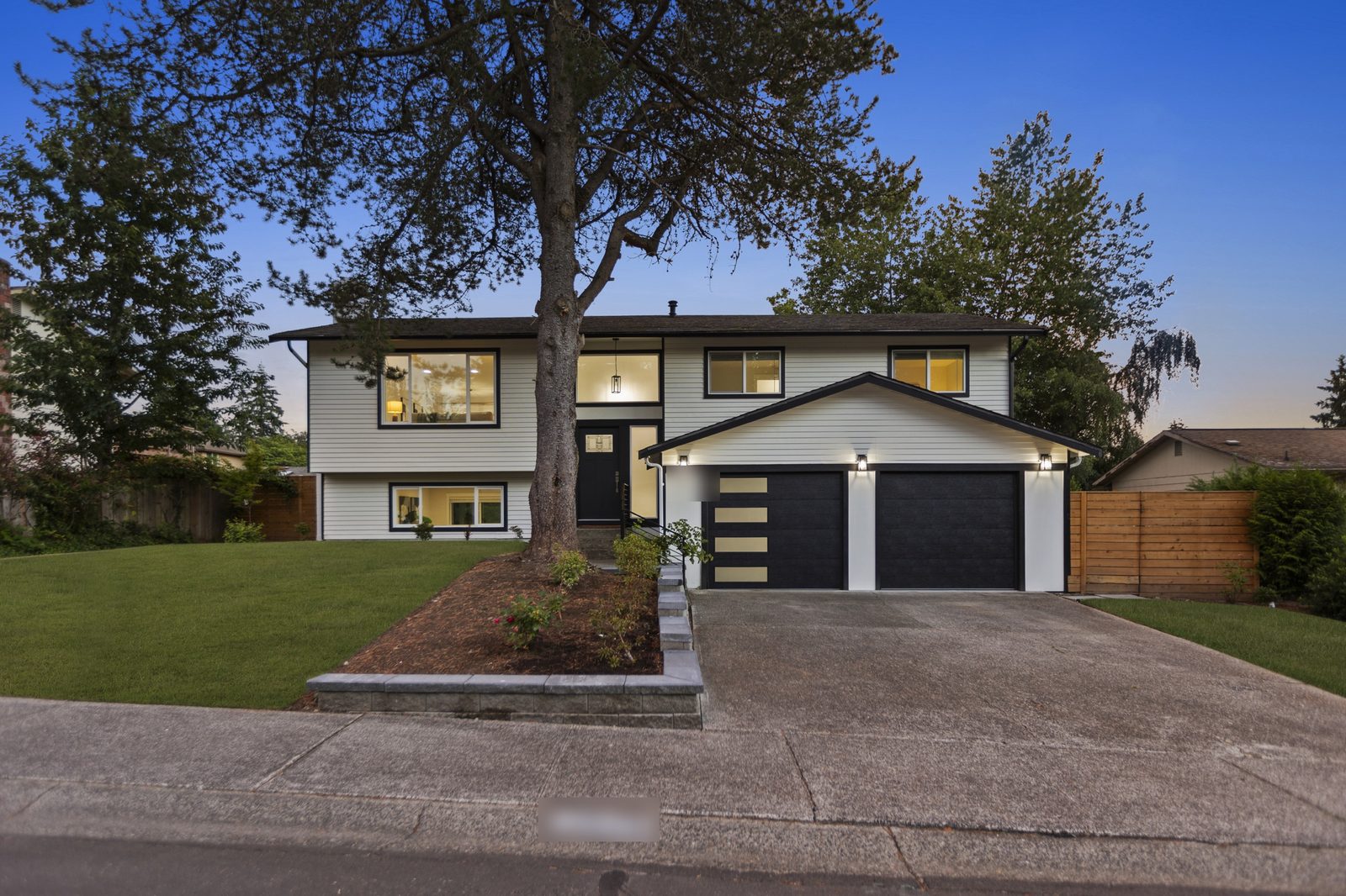 White split level home with black garage doors at dusk